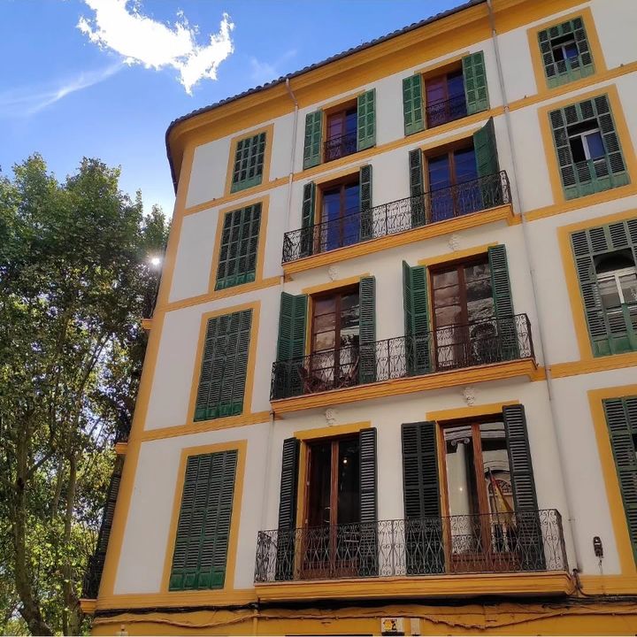 Fachada blanca con marcos amarillos y persianas verdes